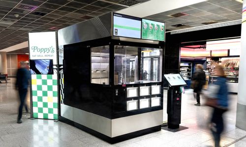 In einem Flughafen steht ein Rochroboter und daneben ein Schild mit der Aufschrift Poppy’s.