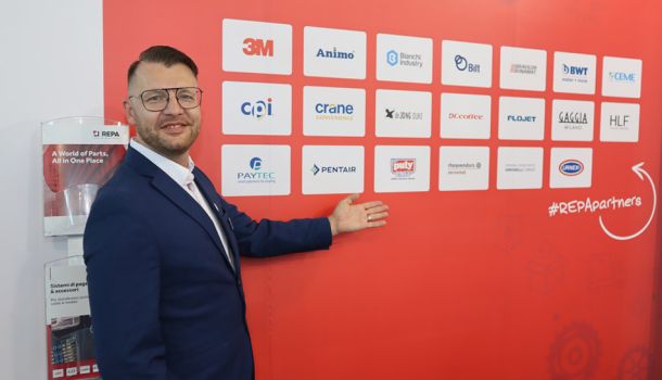 Ein Repa-Mitarbeiter zeigt auf eine Wand mit Firmenlogos.