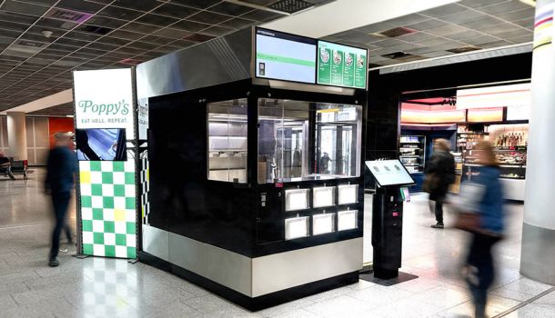 In einem Flughafen steht ein Rochroboter und daneben ein Schild mit der Aufschrift Poppy’s.