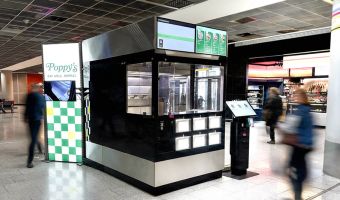 In einem Flughafen steht ein Rochroboter und daneben ein Schild mit der Aufschrift Poppy’s.